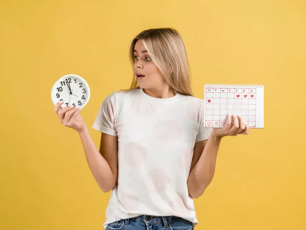 Periode zu früh: Frau schaut überrascht auf Uhr und Zykluskalender bei unerwartetem frühen Periodenbeginn
