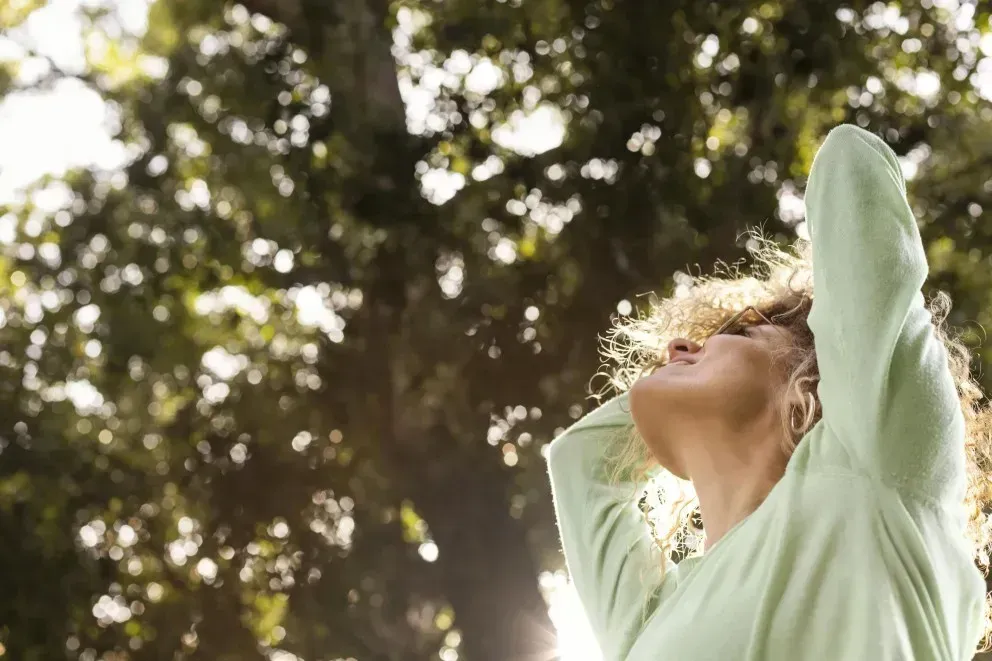 Frau steht in Natur und blickt glücklich nach oben als Symbol für Vitamin B und Zink verändern das Leben