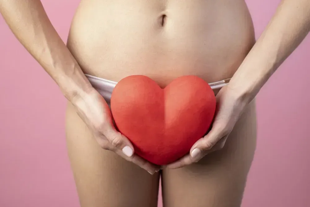 Person hält ein rotes Herz vor dem Unterbauch – Symbol für Zyklusgesundheit, Gebärmutter und Fruchtbarkeit im Zusammenhang mit Prämenstruellem Spotting