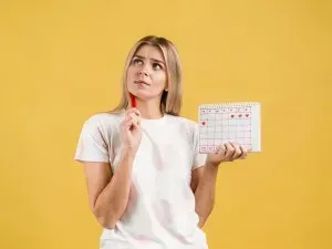 Frau hält einen Menstruationskalender in der Hand und blickt nachdenklich zur Seite – Symbol für Zyklusbeobachtung und möglichen LH-Anstieg sowie Eisprungplanung.