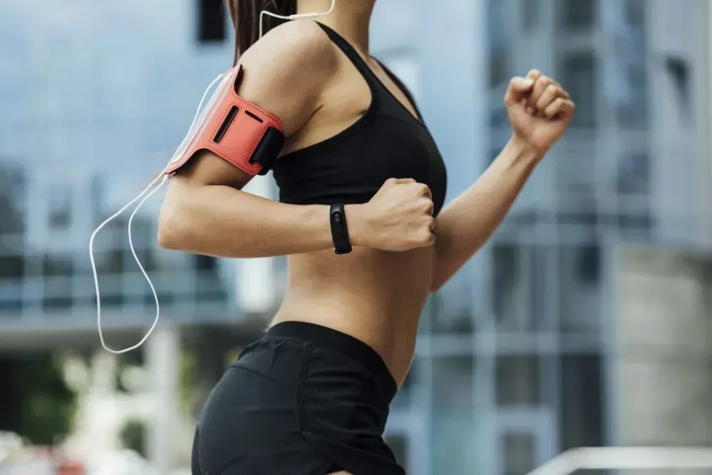 Frau in Sportkleidung joggt im Freien mit Fitnessarmband – Symbol für Bewegung, gesunden Lebensstil und Abnehmen trotz Pille