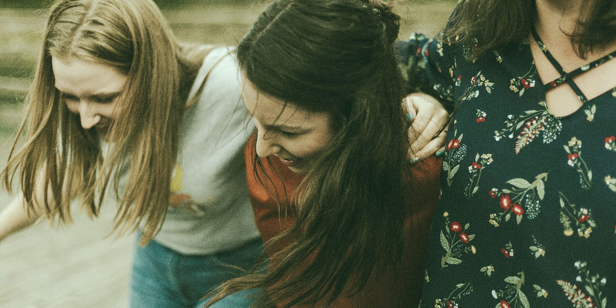 Three women walking together closely, laughing and supporting each other, symbolizing friendship and emotional connection.