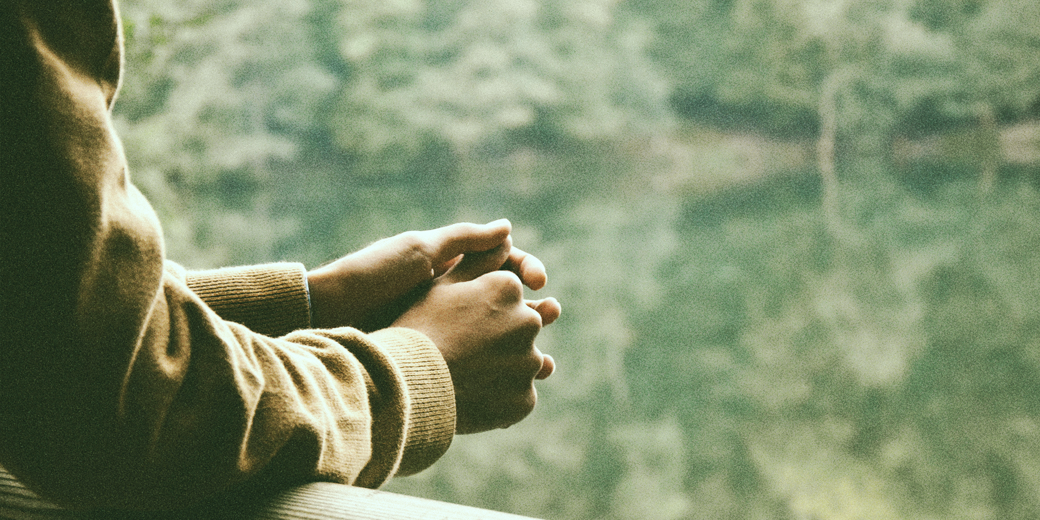 Close-up of hands clasped together, resting on a wooden surface, with a blurred green forest in the background, symbolizing reflection on PMDD and Thyroid.