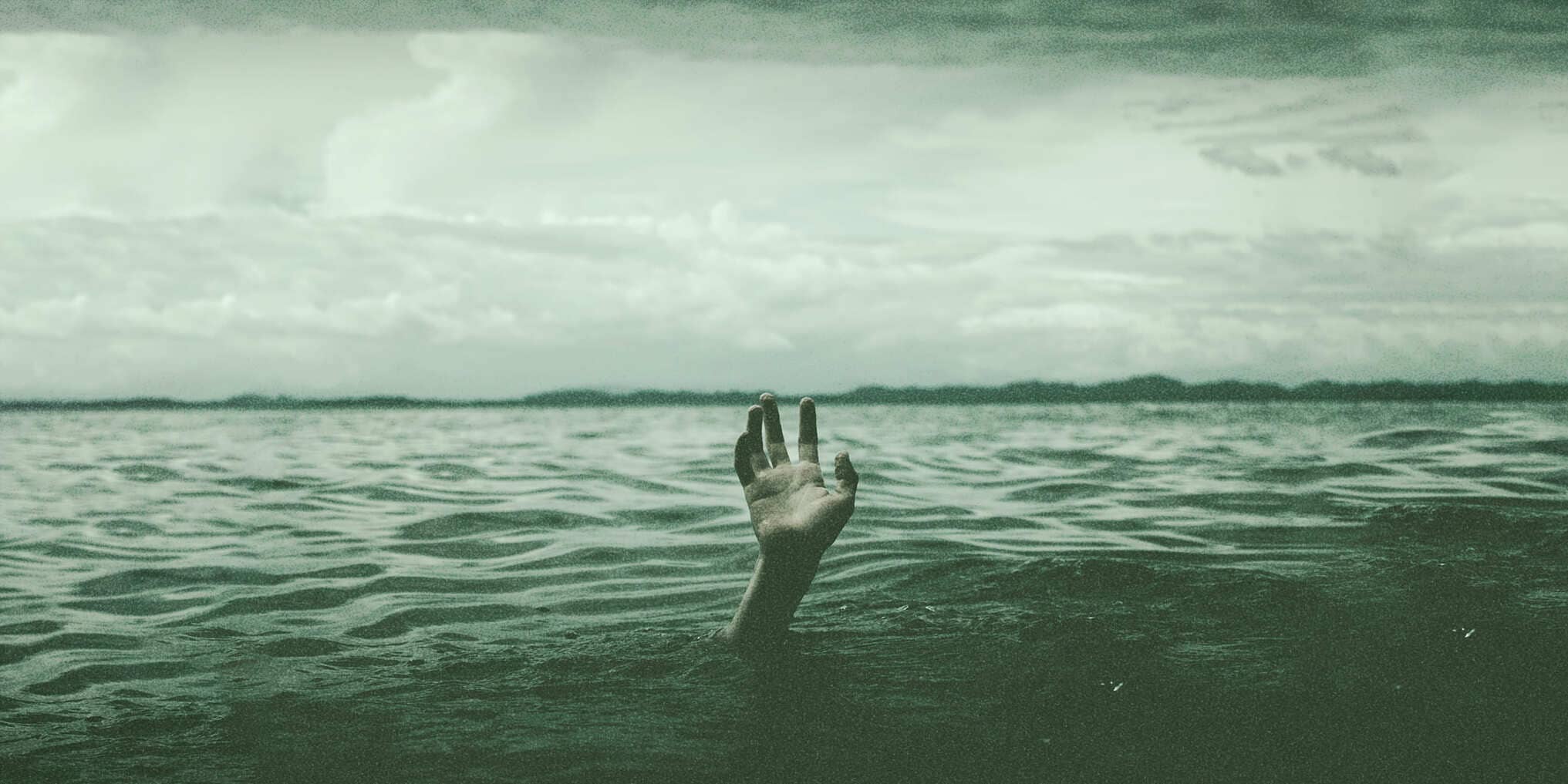 A single hand emerging from a vast body of water, fingers stretched upward, as though signaling for help for pmdd irritability. The atmosphere is muted with shades of green, evoking a feeling of isolation and struggle under an overcast sky.