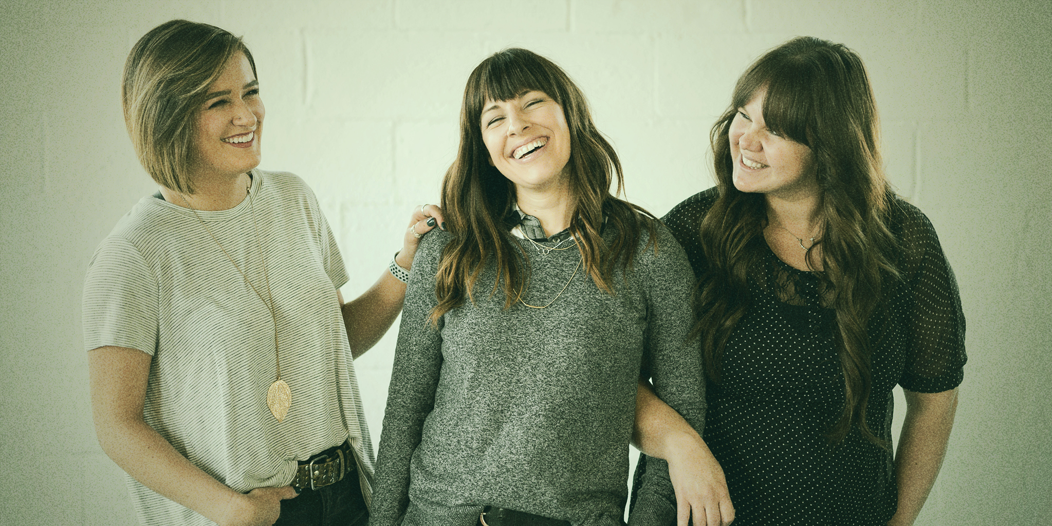 Three women smiling and standing together in a supportive and relaxed manner, symbolizing the importance of fostering workplaces that provide PMDD accommodations.