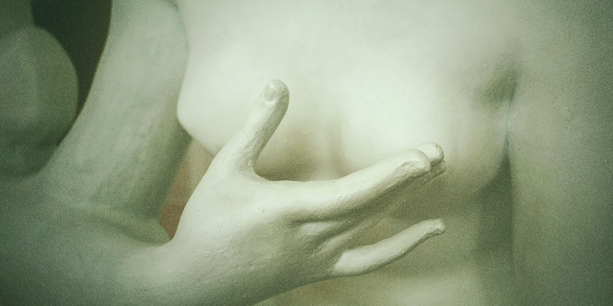 A close-up of a sculpted hand gently resting near a chest, symbolizing tenderness and sensitivity associated with breast discomfort during ovulation.