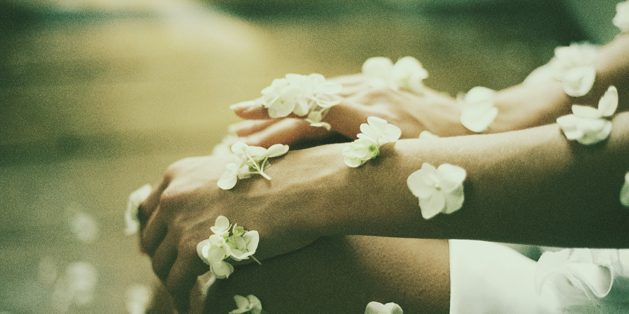 Close-up of hands and arms adorned with delicate white flowers, symbolizing Dry Skin Before Period, set against a softly blurred background with a greenish tint.