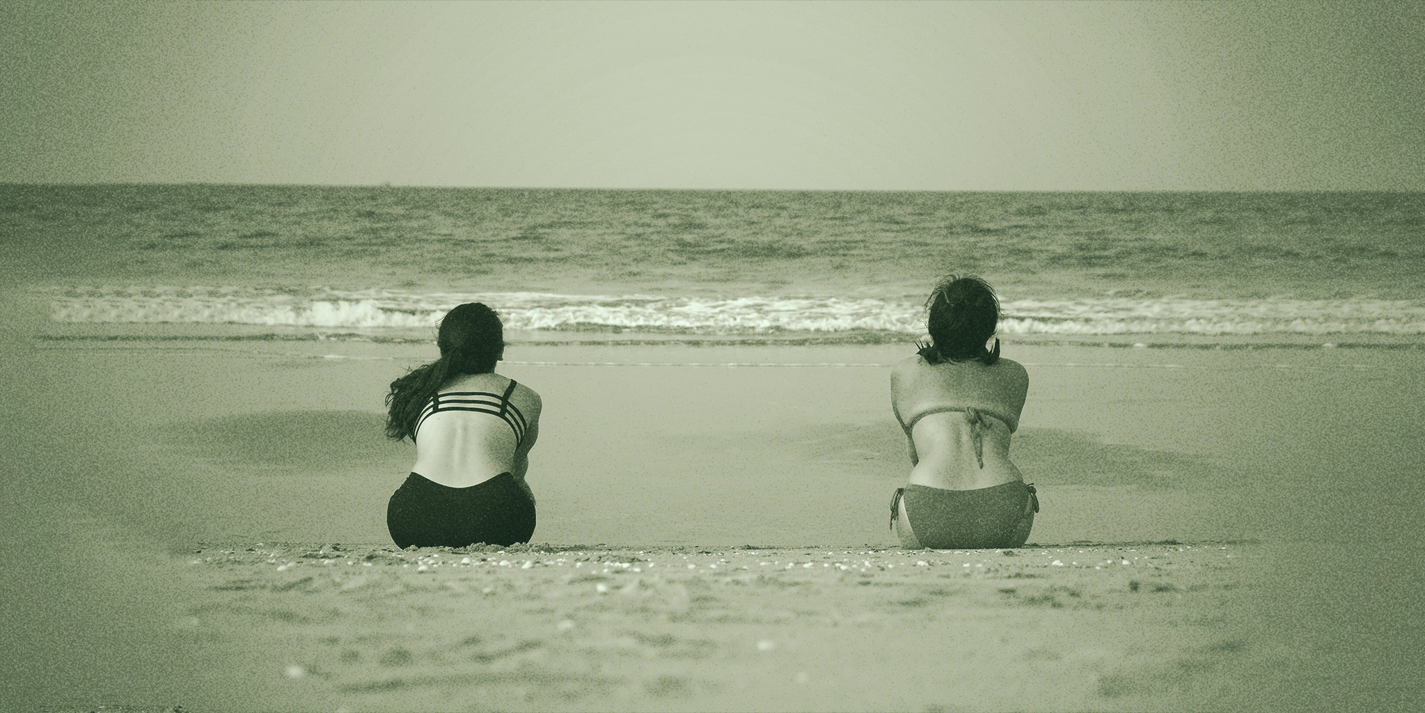 Two women sitting side by side on a calm beach, gazing at the ocean, symbolizing reflection and the nuanced experiences of PME vs PMDD.